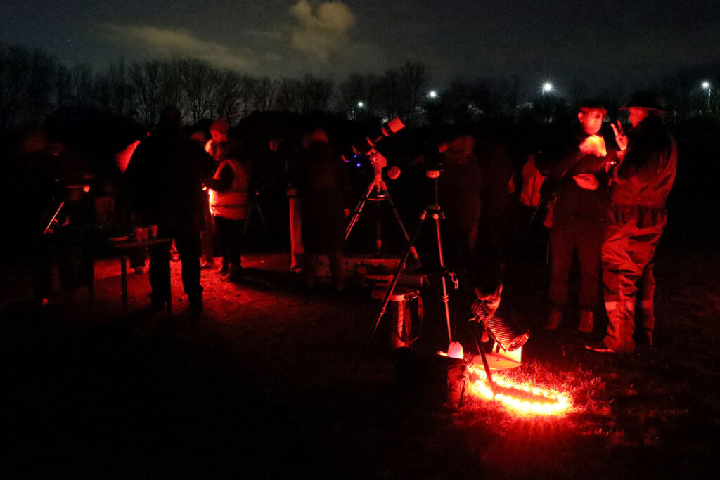 Wide shot telescope set ups on the field, with people engaging in stargazing.