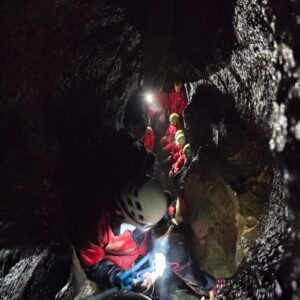 Group of students gathered at the bottom of a cave, one student making the journey down with a harness at the CCF 2024 Training Camp.