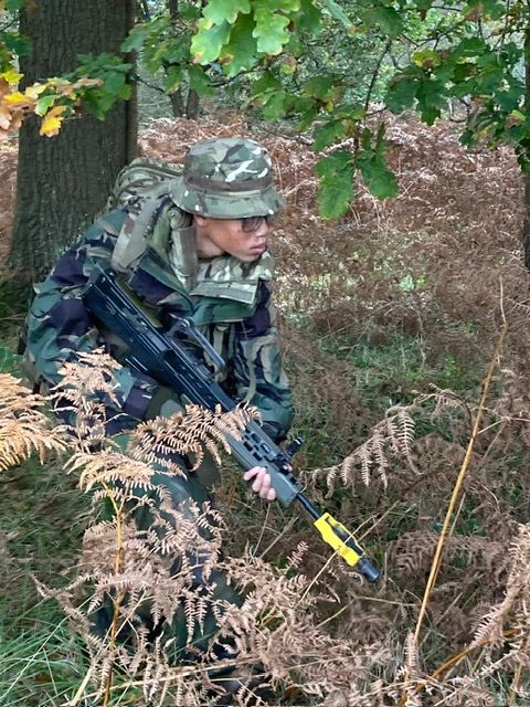 Student with rifle keeping low in the bushes.