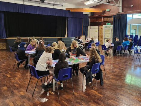 Wide shot of the School Hall with tables of Students and representatives from Brighton Uni playing the Uni Game.