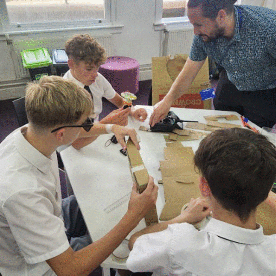 Students working on a task around a table using cardboard and stationary.