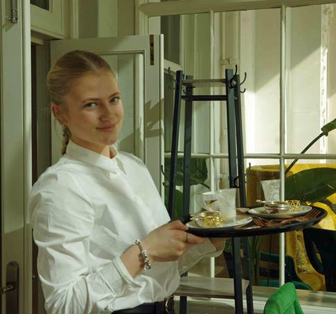 Student posing with a tray, serving tea.
