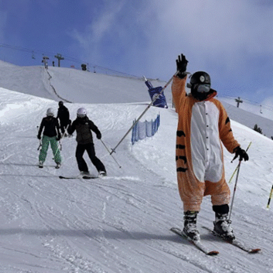 Student skiing down slope waving to the camera.