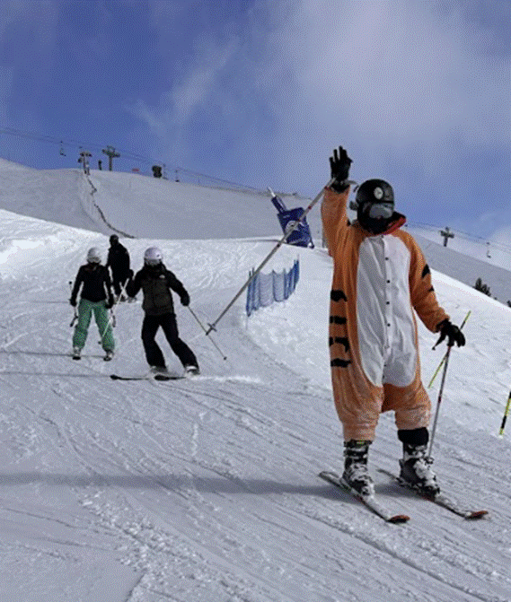 Student skiing down slope waving to the camera.